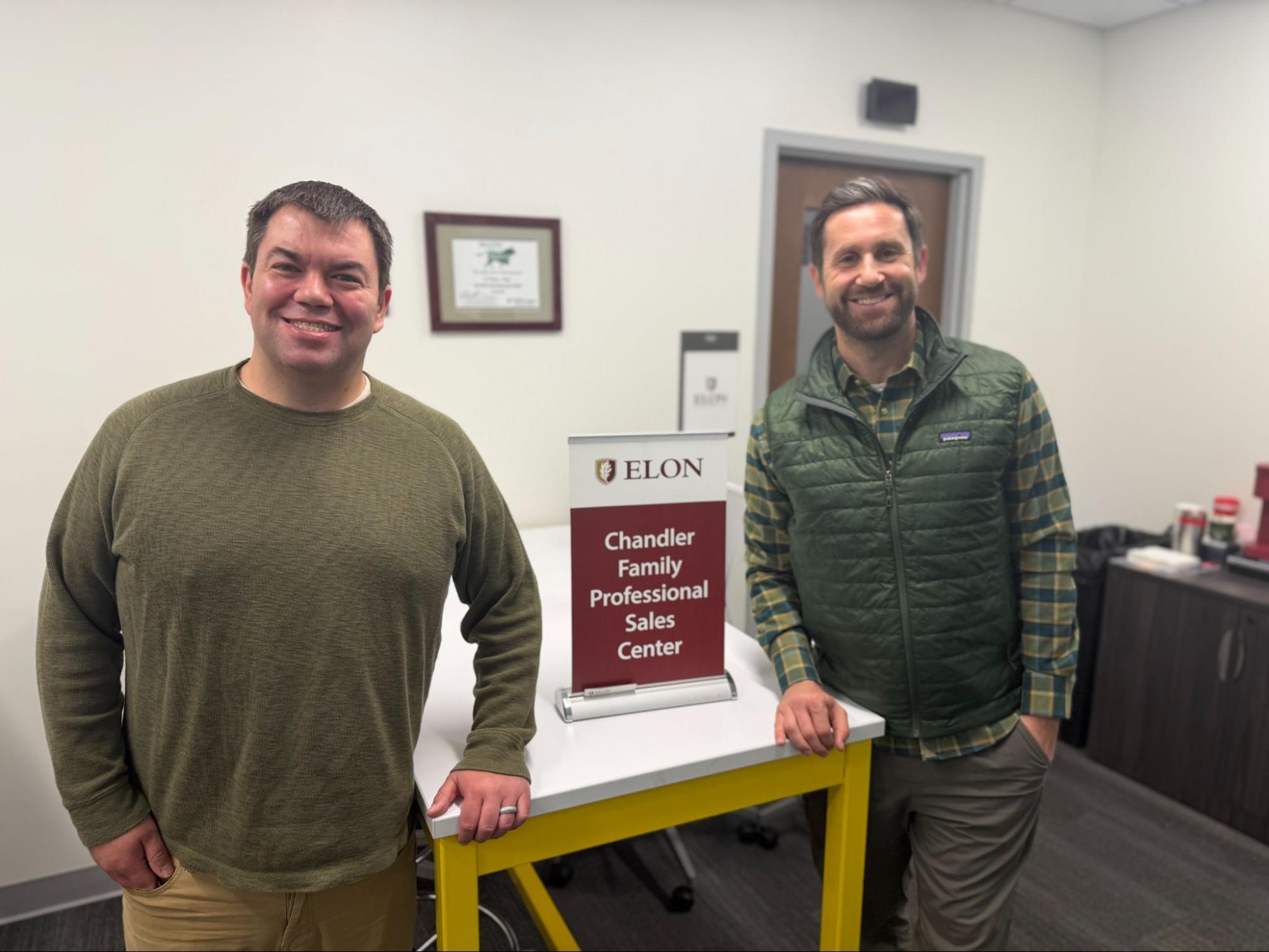 Two men standing by a sales center sign.